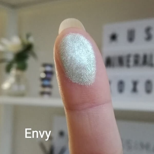 Minerale oogschaduw Envy: licht metallic groene oogschaduw met zachte glans op een vinger tip.